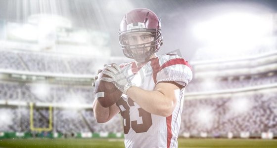 灯光室内背景摄影照片_一名四分卫美式橄榄球运动员在大型现代体育场上投球，灯光和照明弹林立