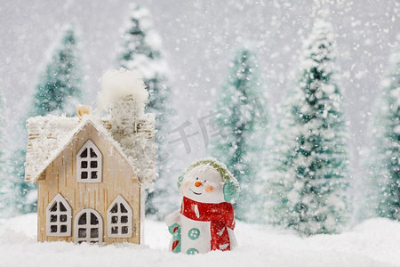 小装饰雪人附近的木屋在冷杉林下落雪。冬天的雪人和房子