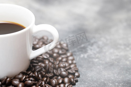 白色咖啡杯和深色咖啡豆放在桌子上，裸露的砂浆水泥风格阁楼背景。柔和的焦点。