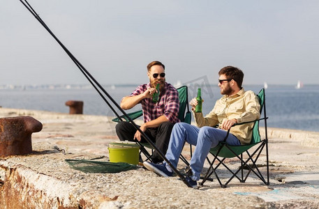 休闲与人的概念-快乐的男性朋友在码头钓鱼和喝啤酒。男性朋友在码头钓鱼和喝啤酒
