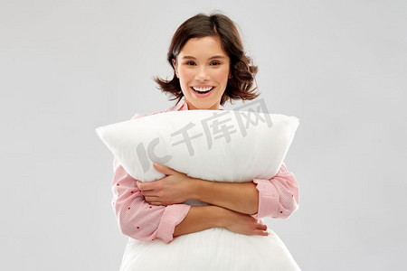 舒适睡眠摄影照片_人和就寝时间概念—睡衣拥抱枕头愉快的年轻妇女在灰色背景快乐的年轻女人在睡衣拥抱枕头