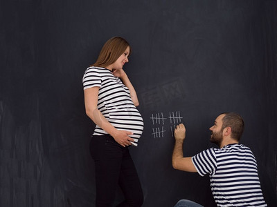 怀孕的夫妇怀孕一周。一对年轻的怀孕夫妇在黑板上用粉笔写下怀孕周