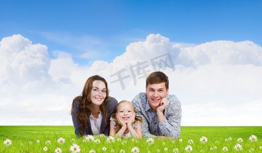 年轻的家庭。幸福的三口之家躺在绿草