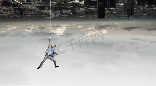 一位年轻的商人吊在城市上空的绳子上。一名男子挂在绳子上