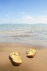 沙滩拖鞋摄影照片_沙滩上的黄色沙滩拖鞋，夏天，洗澡