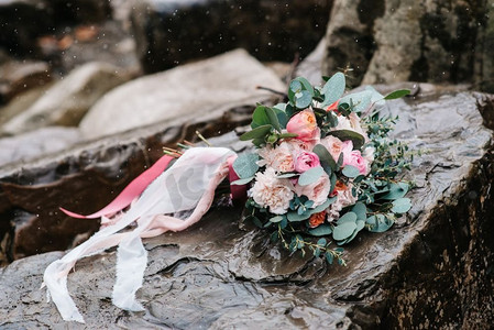 蓝色装饰彩带摄影照片_牡丹结婚花束，石头上系着彩带，特写，S在下雪