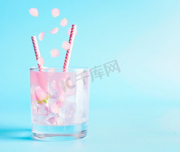 蓝色冰丝摄影照片_带有玫瑰花瓣和花朵的夏日饮料。点心饮料。蓝底冰柠檬水或鸡尾酒