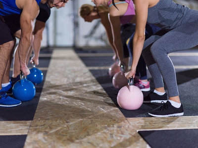 一群健康的年轻运动员在Cross健身工作室用壶铃进行锻炼。运动员拿着壶铃做运动