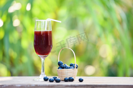 蓝莓奶昔果汁玻璃杯和篮子里的新鲜蓝莓水果，以自然绿色的夏日为背景