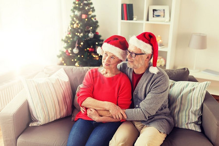 圣诞节，假日和人的概念—在家里的圣诞老人帽子快乐微笑的高级夫妇。圣诞老人帽快乐的老年夫妇