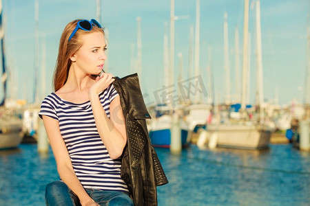 旅游休闲与人的理念。戴着蓝色心形太阳镜的时尚金发女孩在码头与港口的游艇对峙