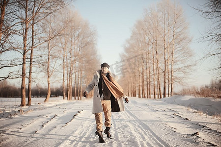冬季风格摄影照片_穿着大衣/冬季风格的时髦男子，在冬季风景的背景下行走，下雪的天气，保暖的衣服