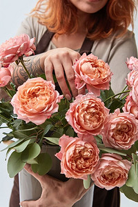 手上有纹身的年轻女孩拿着一个粉红玫瑰花瓶。鲜花店概念一个穿着围裙的女孩手里拿着一支玫瑰