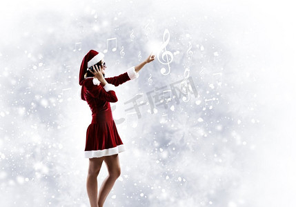 庆祝新年。年轻漂亮的圣诞老人女孩戴着耳机听音乐