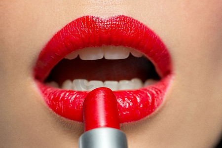 红色口红嘴唇摄影照片_美容、化妆和化妆品概念--女人在嘴唇上涂上红色唇膏的面部特写。一名女子在嘴唇上涂上红色口红的特写