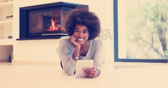 搜索秋天摄影照片_秋天，美丽的年轻黑人妇女在她的豪宅壁炉前的地板上使用平板电脑