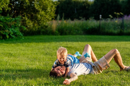 快乐的男人和孩子在草地上享受户外乐趣。公园里父子俩在绿茵茵的草地上休息的家庭生活场景。