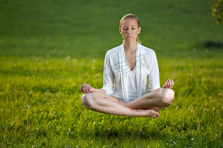 瑜伽美容摄影照片_穿白衣的女人在做瑜伽，在草坪上翱翔。瑜伽