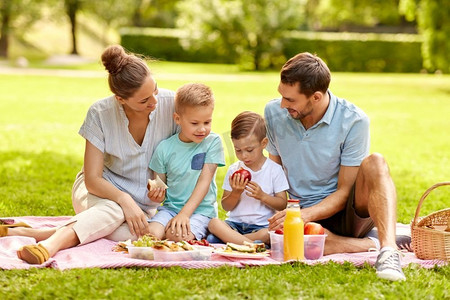 家庭、休闲和人的概念-快乐的母亲、父亲和两个小儿子在夏季公园野餐。快乐的一家人在夏季公园野餐