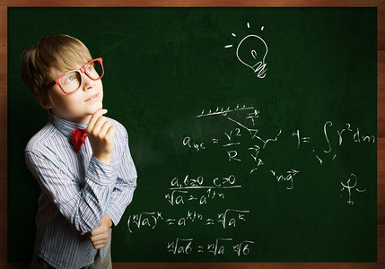 聪明的小学生。戴着红眼镜的聪明男孩在黑板上写着公式