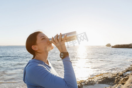 出水素果摄影照片_女人在海滩上喝水。年轻女子饮用水后行使在海滩上