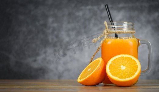 新鲜水果片摄影照片_橘子汁在玻璃罐和新鲜的橘子水果片在木桌/静物玻璃汁黑暗与拷贝空间背景