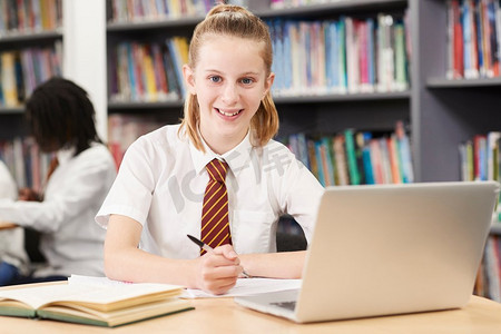 女高中生摄影照片_肖像的女高中生穿着制服工作在笔记本电脑在图书馆
