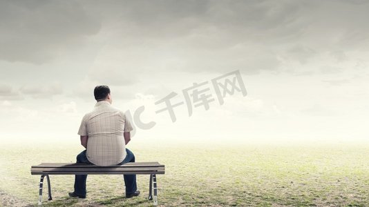 板凳摄影照片_胖子背着背坐在板凳上，目光转向别处。胖子