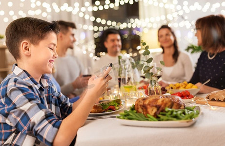 科技、假期和人的概念快乐的男孩带着智能手机在家里开家庭晚宴。在家庭晚宴上拿着智能手机的男孩