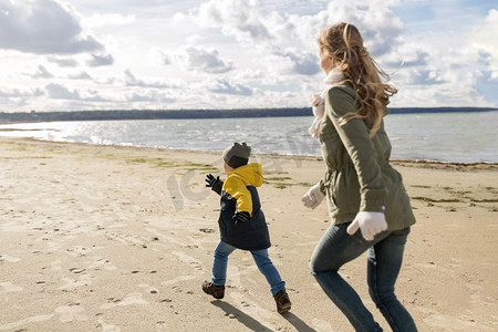 家庭、休闲、人的概念-快乐的父母和小儿子沿着秋天的海滩奔跑。幸福的一家人沿着秋天的海滩跑步
