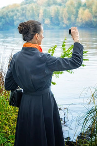 优雅的高级女商人与一个数码相机，一个包和橙色围巾，拍照沿河