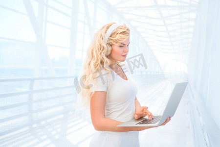 美丽的年轻女子戴着耳机听音乐，通过笔记本电脑上网，在线购买音乐。