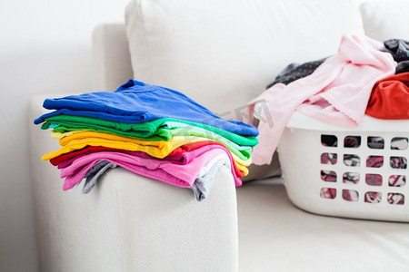 干净的棉花摄影照片_在篮子里洗衣服，在沙发上放一叠干净的亚麻布。五颜六色的干净衣服