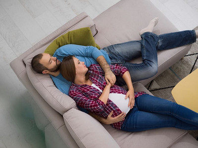 怀孕的夫妇摄影照片_怀孕的夫妇在沙发上放松。顶视图愉快的怀孕夫妇放松在沙发在家里