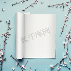 模拟打开的杂志或目录，背景为淡蓝色桌面，有树枝和白色樱花，俯视，平铺