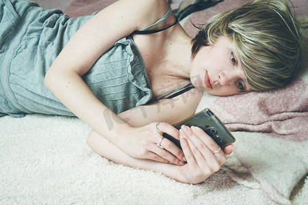  年轻的金发女郎在她的床上使用她的智能手机                              