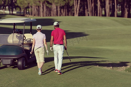 一对年轻夫妇在高尔夫球场上走向下一个球洞。一个拿着高尔夫球包的男人。走在高尔夫球场上的情侣
