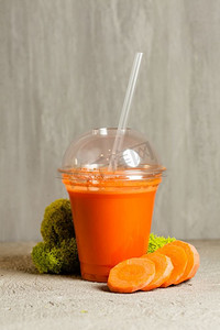天然凉爽摄影照片_塑料杯胡萝卜汁和新鲜蔬菜放在一起。胡萝卜汁