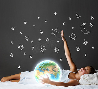 晚上做梦。可爱的女孩睡在床上，看着地球行星。这张图片的元素是由美国宇航局提供的