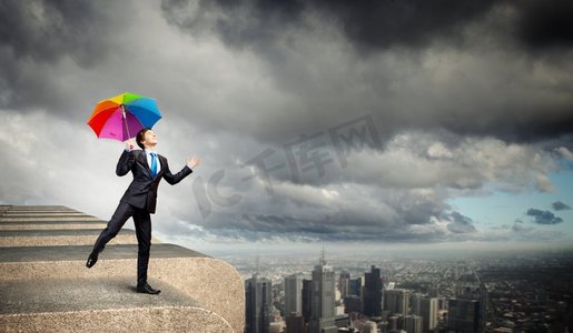 楼顶撑着伞的商人。一位穿着黑色西装、撑着雨伞的商人站在楼顶