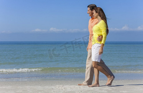 夏天衣服摄影照片_身穿五颜六色衣服的男女浪漫情侣漫步在蔚蓝蓝天的荒凉热带海滩上