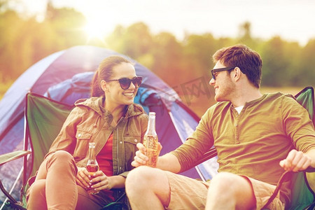 喝啤酒摄影照片_露营、旅行、旅游、徒步旅行和人类概念-在露营帐篷里喝啤酒或苹果酒的幸福夫妇。幸福的情侣在露营帐篷里喝啤酒