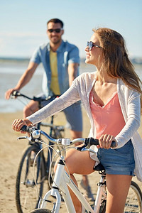 人，休闲，生活理念-快乐的年轻夫妇在海滩上骑自行车。幸福的年轻夫妇在海边骑自行车
