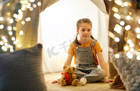 童年和hygge概念—快乐的小女孩与玩具在孩子帐篷在家里。小女孩与玩具在孩子帐篷在家里