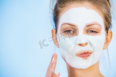 年轻女子与白色干泥面具在脸上，反对蓝色。青少年女孩检查治疗结果。护肤品女孩与干白色泥面膜在脸上