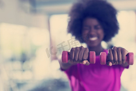 crossfit摄影照片_快乐健康的非裔美国女性在CrossFit健身房用哑铃减肥。一名女子戴着哑铃在CrossFit健身房锻炼