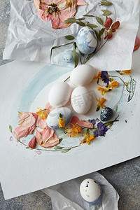 在纸上的白色鸡蛋与花和水彩画在石背景。复活节彩蛋与鲜花装饰