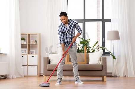 清洁、家务和家政概念—印度男子用扫帚扫地在家里。男人用扫帚打扫地板