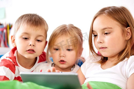 童年、科技和家庭观念--家里的小孩子在床上玩平板电脑。家里的小孩子在床上玩平板电脑