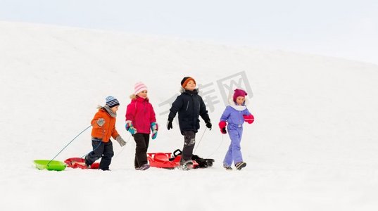 小孩子摄影照片_童年，雪橇和季节概念—一群快乐的小孩子在冬天雪橇。快乐的小孩子与雪橇在冬天